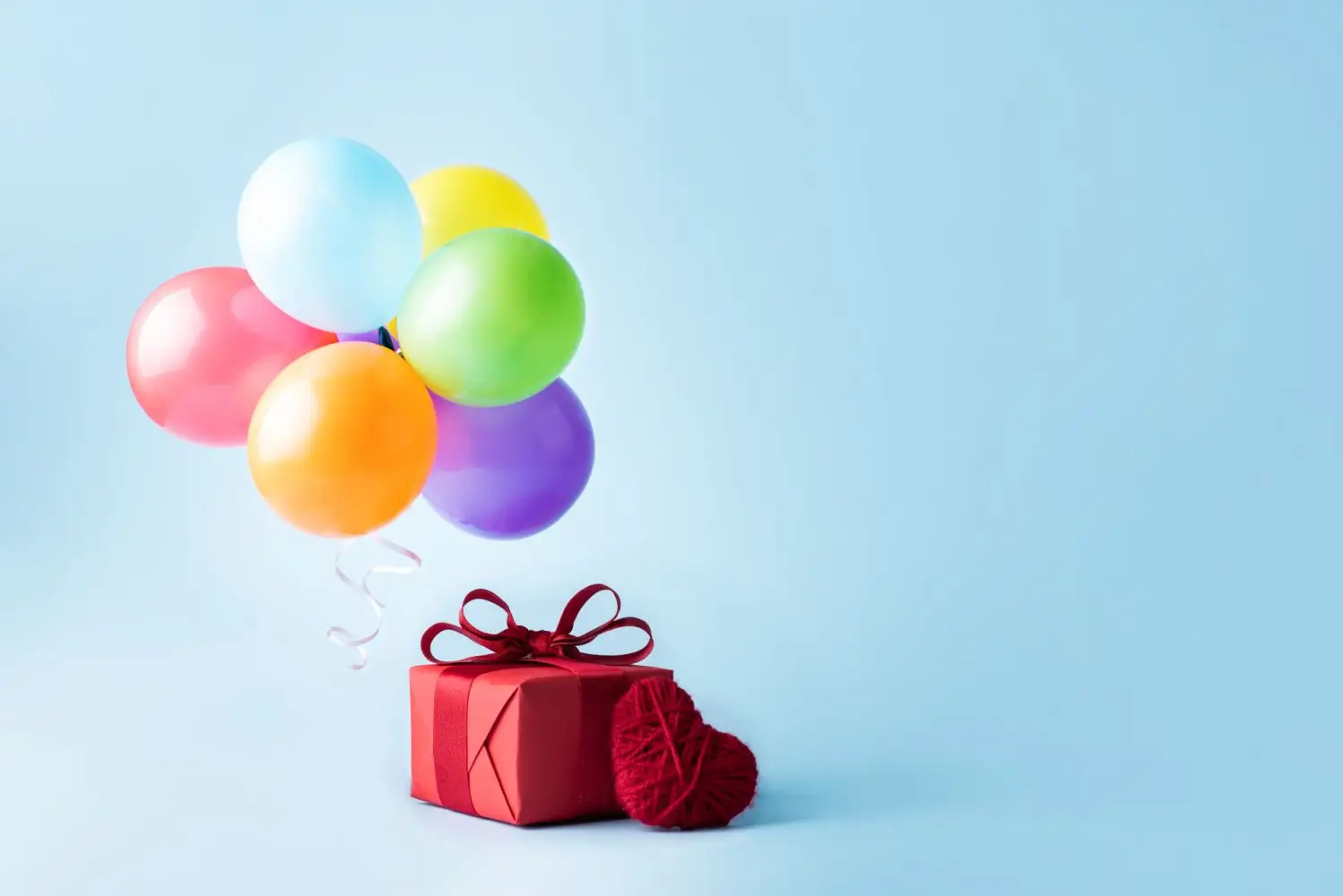 Embrulho de presente vermelho em um fundo azul, com balões de festa amarrados no presente